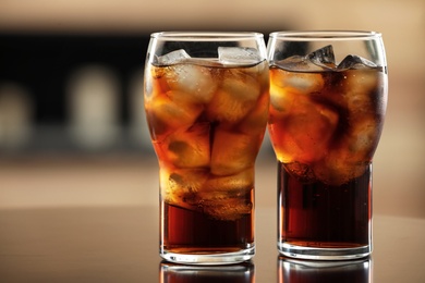 Glasses of cola with ice on table against blurred background