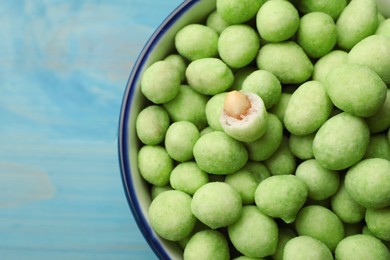 Photo of Tasty wasabi coated peanuts in bowl on turquoise table, top view