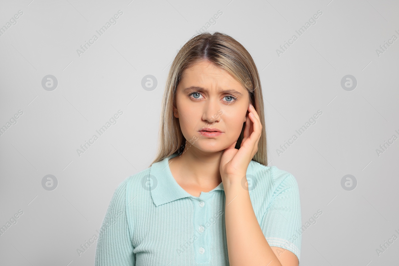 Photo of Young woman suffering from ear pain on light grey background