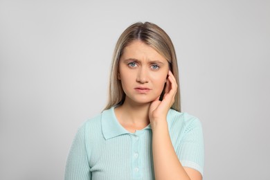 Young woman suffering from ear pain on light grey background