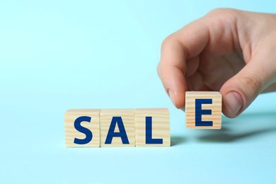 Image of Woman making word Sale with wooden cubes on light blue background, closeup