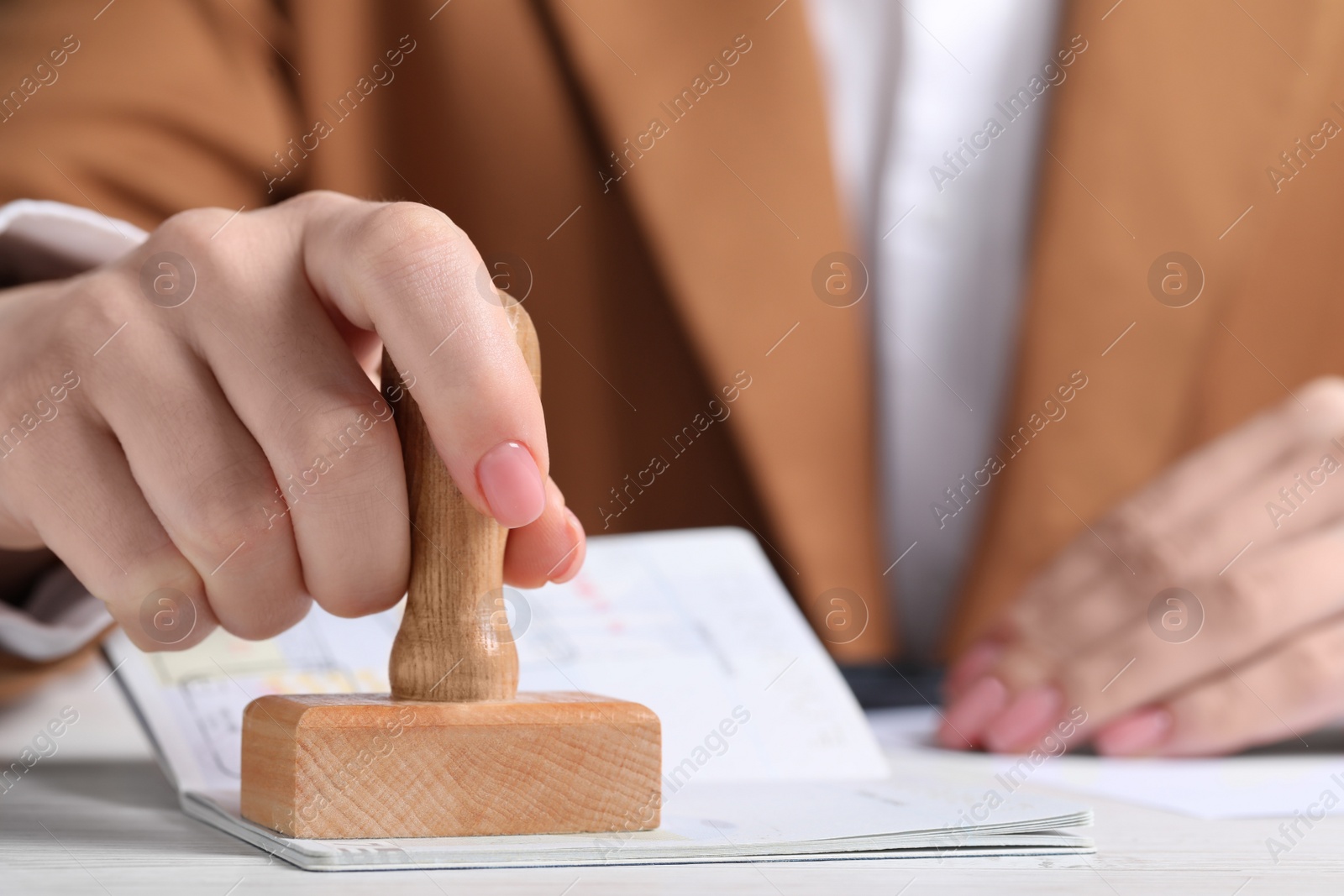 Photo of Ukraine, Lviv - September 6, 2022: Woman stamping visa page in passport at white wooden table, closeup