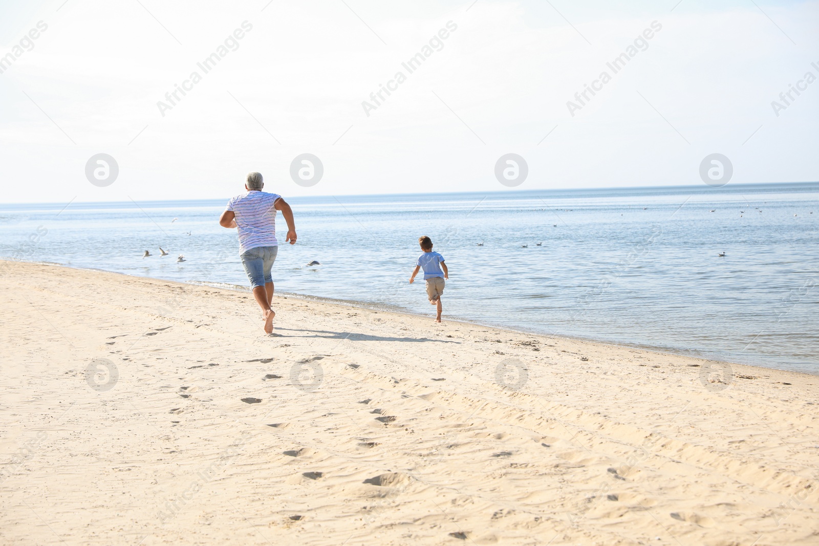 Photo of Cute little boy with grandfather spending time together on sea beach