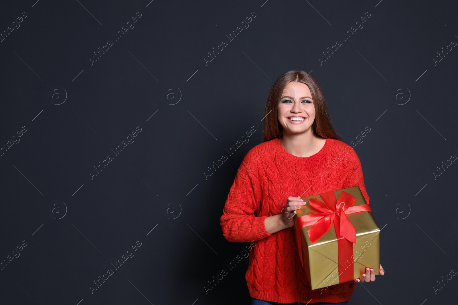 Photo of Young woman with Christmas gift on dark background. Space for text