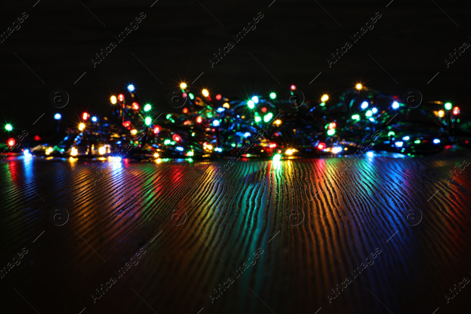 Photo of Beautiful colorful Christmas lights on wooden table. Space for text