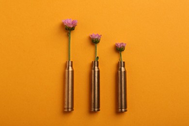 Photo of Beautiful flowers in bullet cases on orange background, flat lay