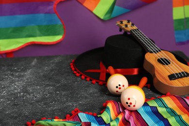 Black Flamenco hat, ukulele, poncho and maracas on dark textured table, closeup. Space for text