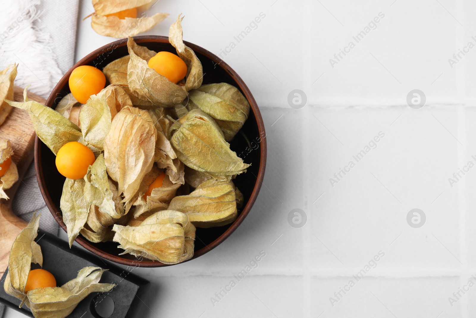 Photo of Ripe physalis fruits with calyxes on white tiled table, flat lay. Space for text