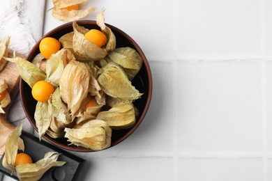 Ripe physalis fruits with calyxes on white tiled table, flat lay. Space for text