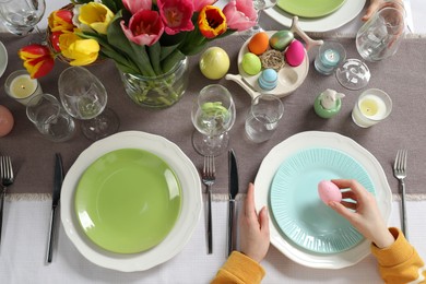 Woman setting table for festive Easter dinner at home, top view