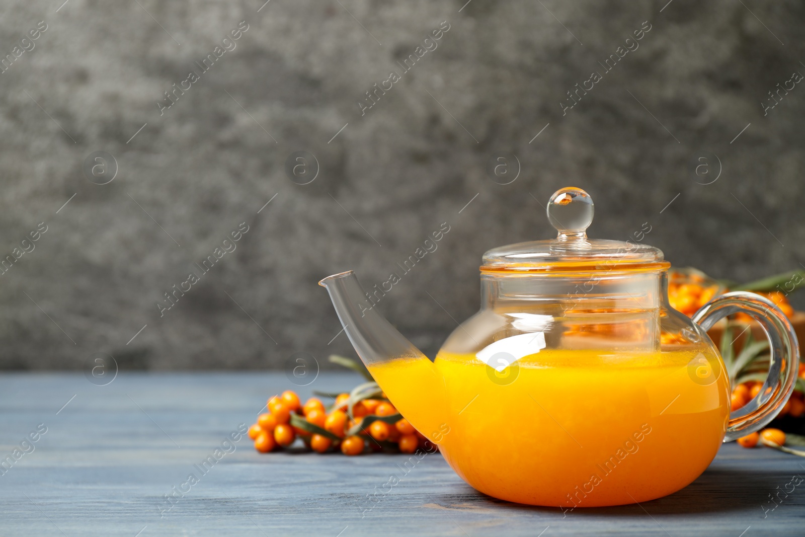 Photo of Delicious sea buckthorn tea and fresh berries on blue wooden table. Space for text