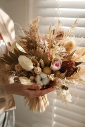Photo of Woman holding beautiful dried flower bouquet near window at home, closeup