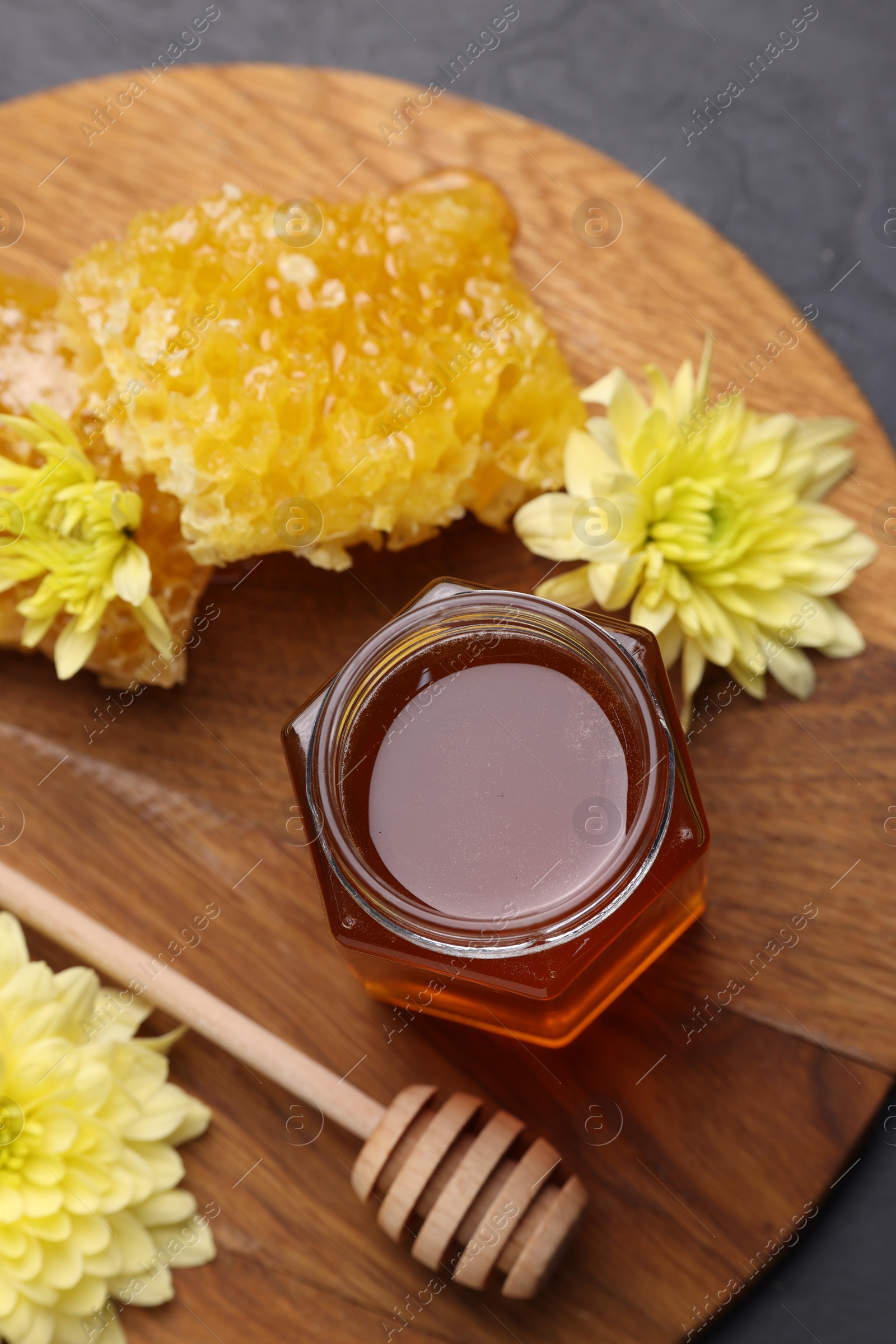 Photo of Sweet honey in jar, dipper, chrysanthemum flowers and pieces of honeycomb on grey table, flat lay
