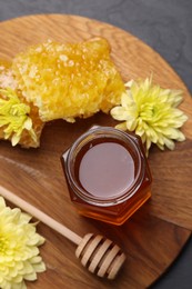 Photo of Sweet honey in jar, dipper, chrysanthemum flowers and pieces of honeycomb on grey table, flat lay