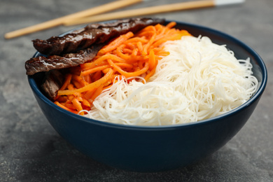 Photo of Tasty cooked rice noodles with meat and carrot on grey table