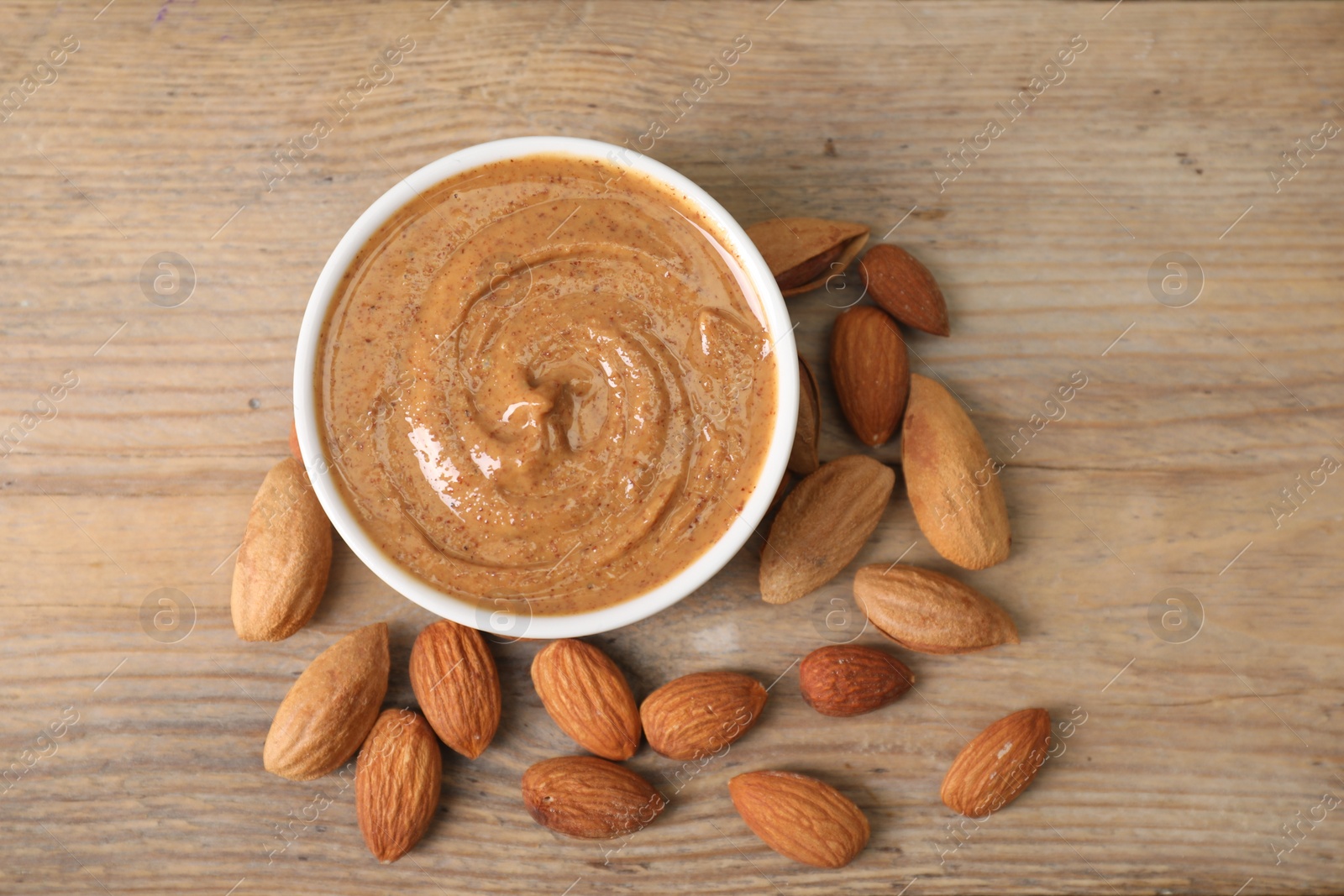 Photo of Delicious nut butter in bowl and almonds on wooden table, top view