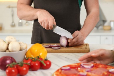 Photo of Man cutting onion near woman in kitchen, closeup. Cooking together