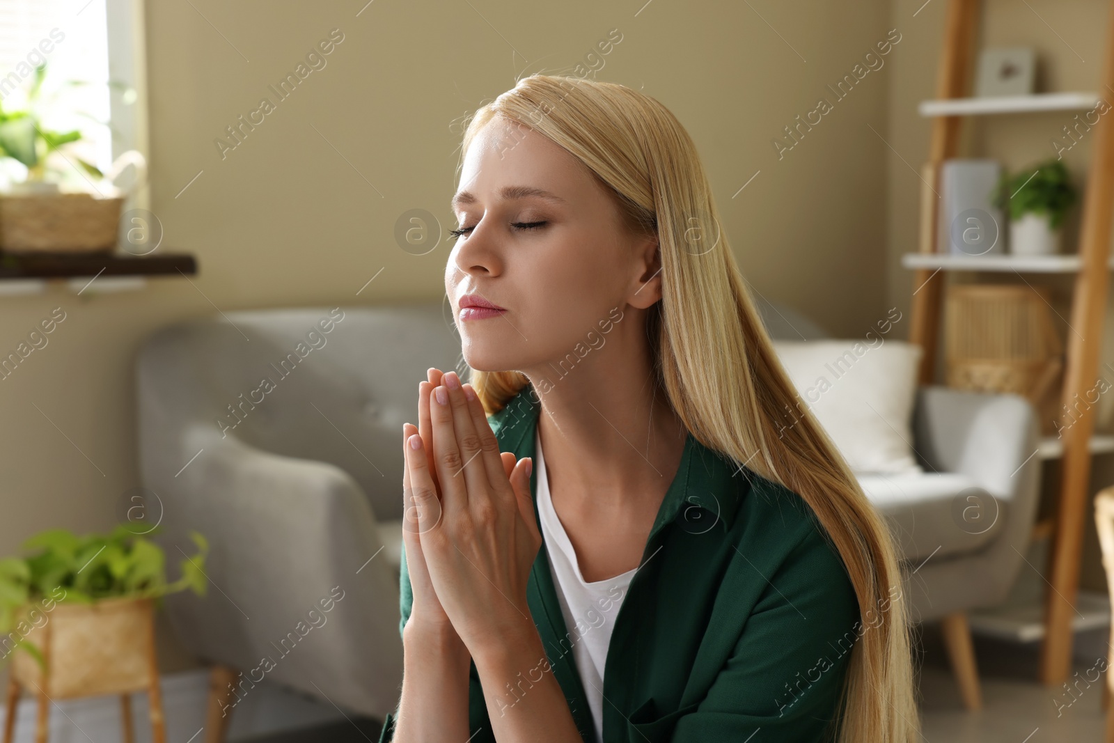 Photo of Religious young woman with clasped hands praying indoors