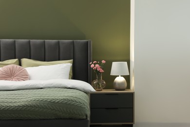Photo of Large comfortable bed, nightstand, lamp and beautiful flowers in stylish room. Interior design