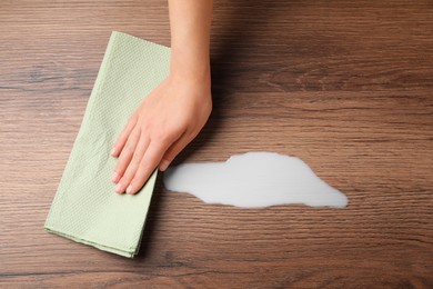 Photo of Woman wiping spilled milk with paper napkin on wooden surface, top view