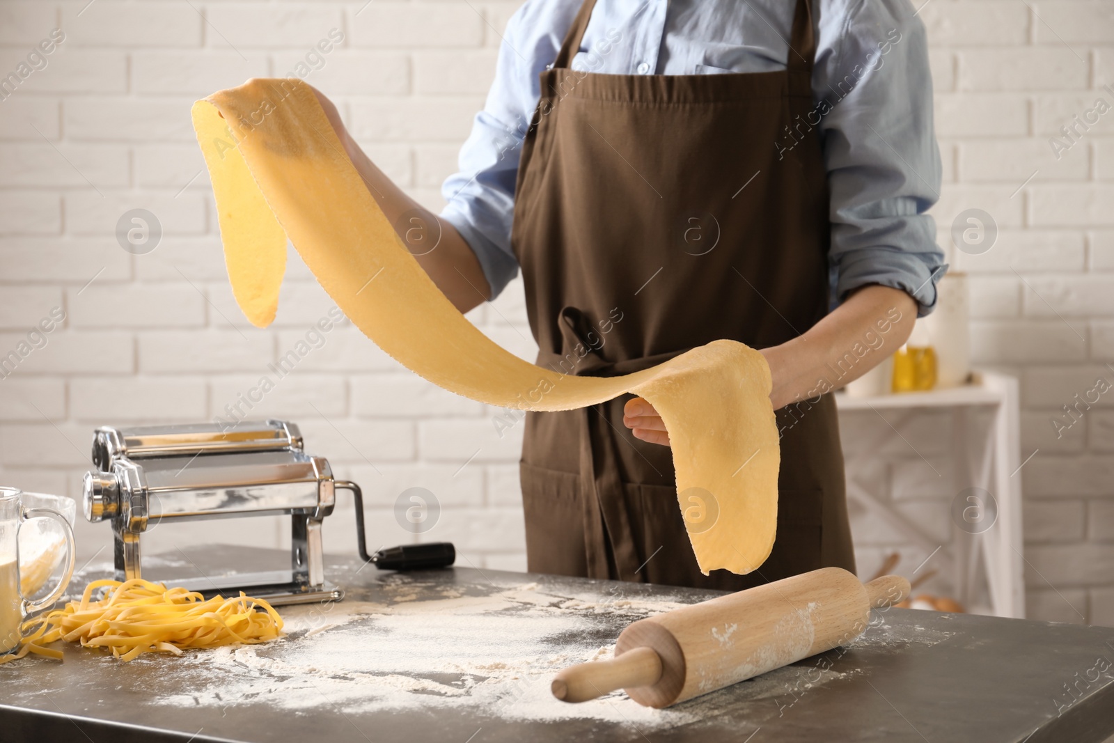 Photo of Young woman preparing dough for pasta at table