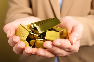 Woman holding shiny gold bars on yellow background, closeup