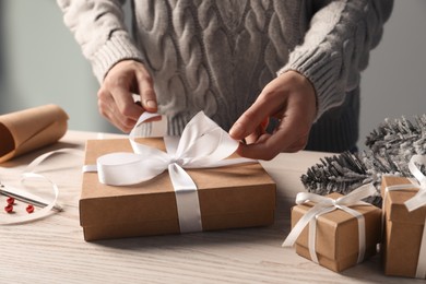 Woman decorating gift box at white wooden table, closeup. Christmas present