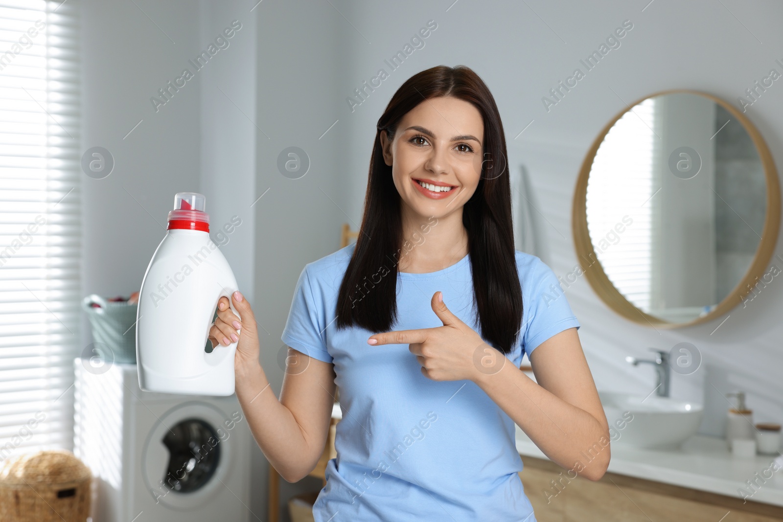 Photo of Beautiful woman showing fabric softener in bathroom