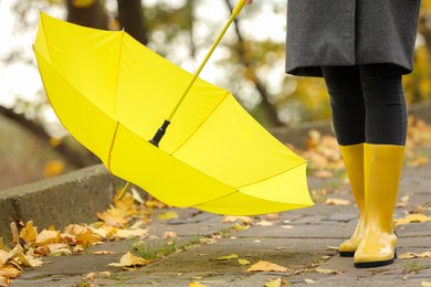 Photo of Woman with yellow umbrella and rubber boots in autumn park, closeup