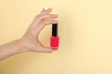 Photo of Woman holding nail polish on beige background, closeup