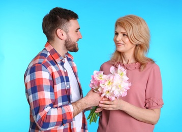 Photo of Young man congratulating his mature mom on color background. Happy Mother's Day