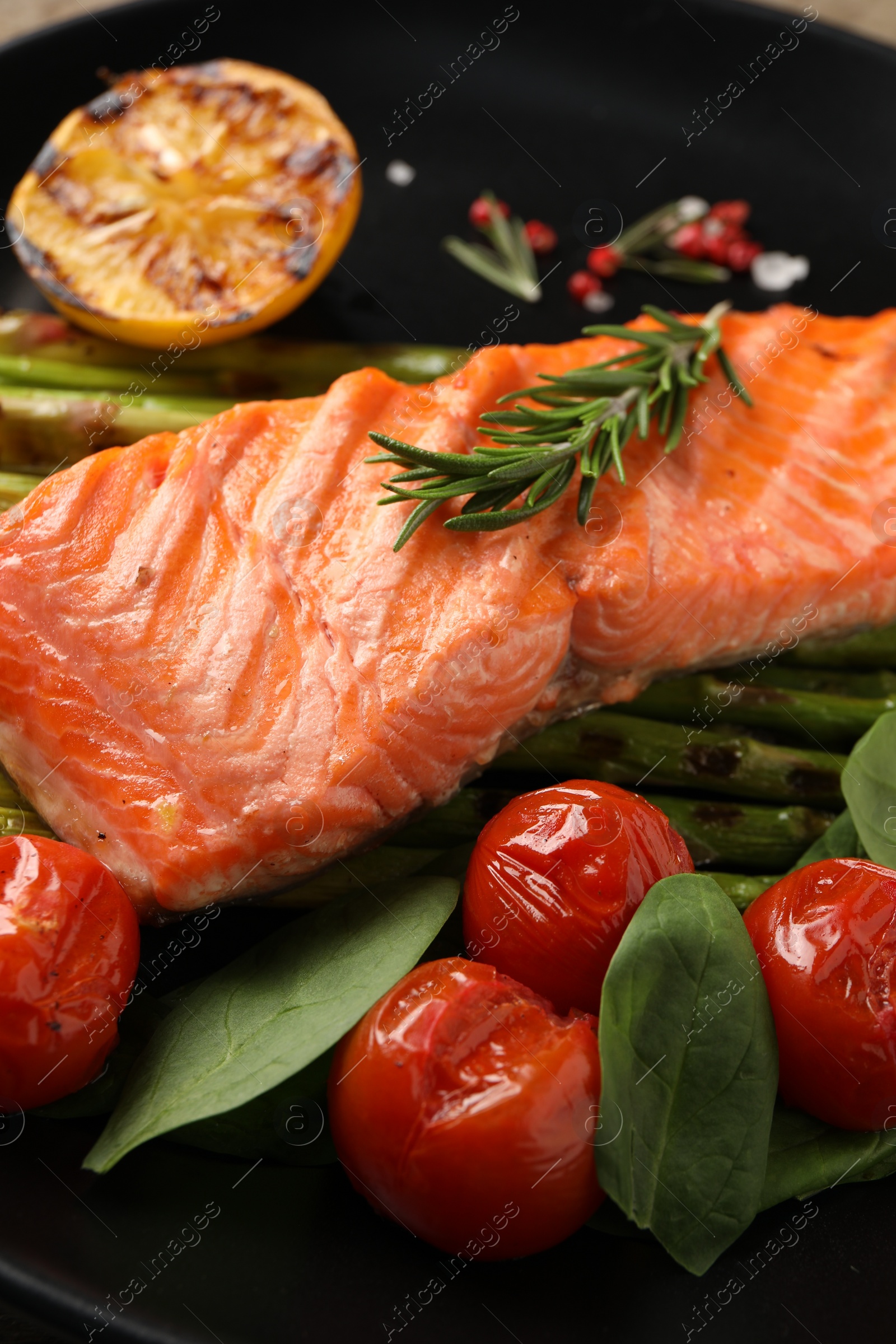 Photo of Tasty grilled salmon with tomatoes, spinach and rosemary on plate, closeup