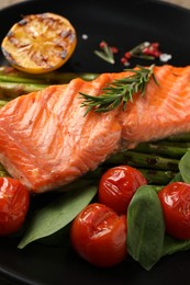 Tasty grilled salmon with tomatoes, spinach and rosemary on plate, closeup