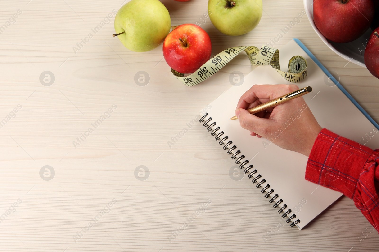 Photo of Woman developing diet plan at light wooden table with apples and measuring tape, top view. Space for text