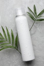 Dry shampoo spray and green leaves on light grey table, flat lay