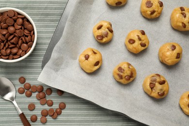 Photo of Baking pan with unbaked cookies and chocolate chips on tablecloth, flat lay