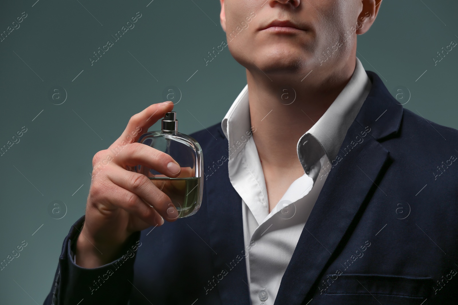 Photo of Handsome man in suit using perfume on dark background, closeup