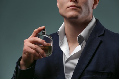 Handsome man in suit using perfume on dark background, closeup