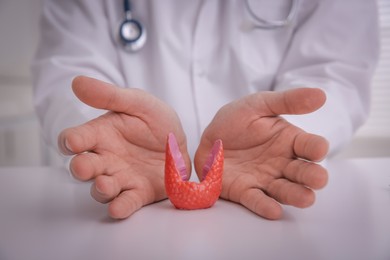 Photo of Doctor with thyroid gland model at table indoors, closeup