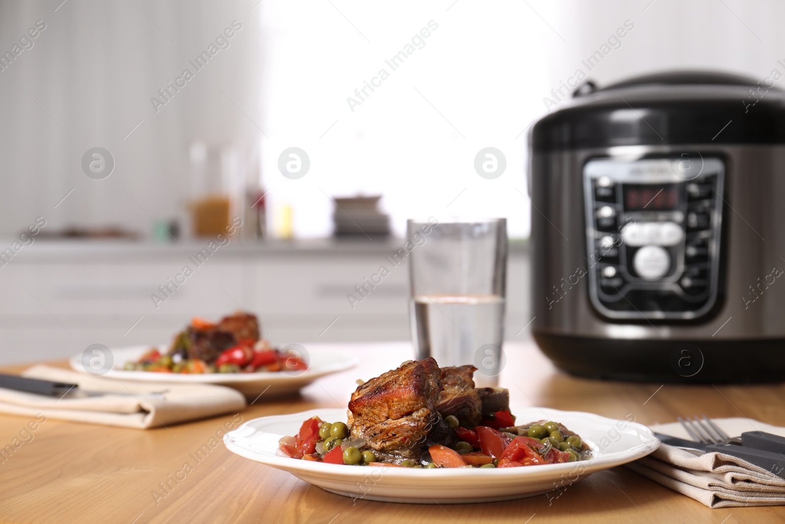 Photo of Plate with meat and garnish prepared in multi cooker on wooden table in kitchen. Space for text