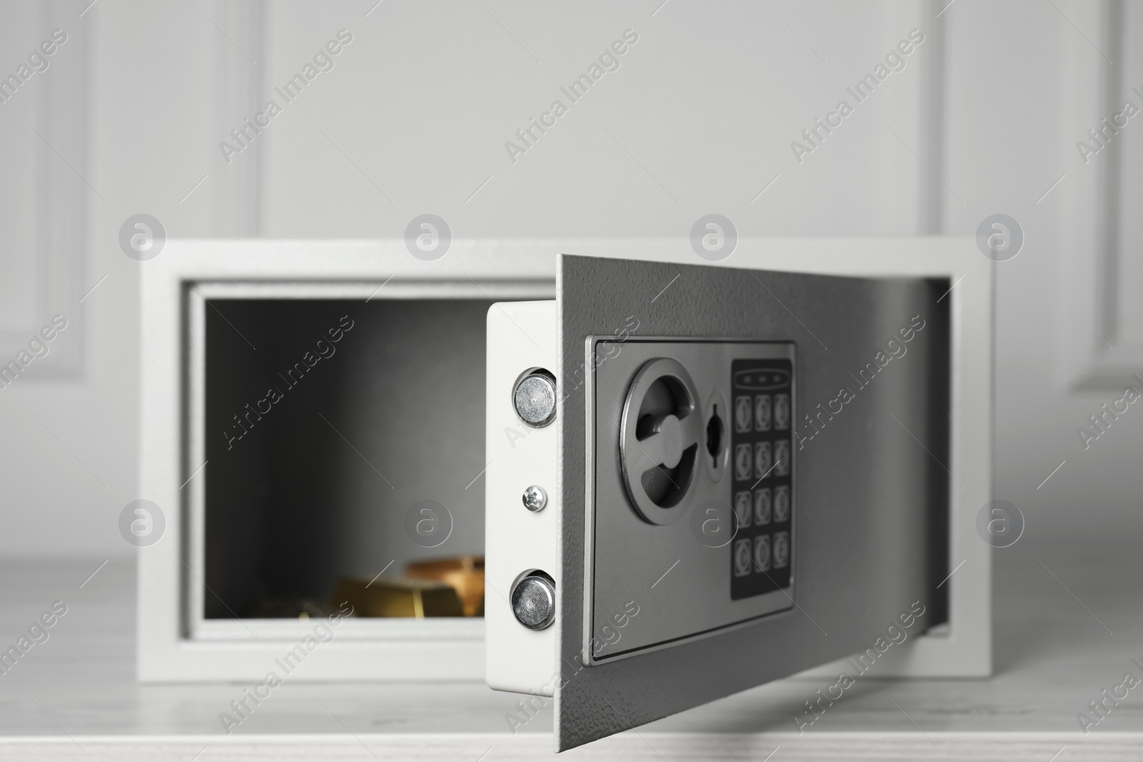 Photo of Open steel safe with gold bar and jewelry on wooden table