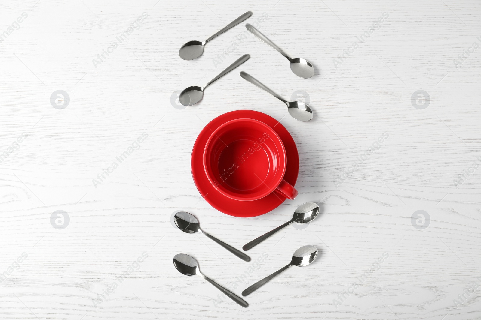 Photo of Flat lay composition with teaspoons and red cup on white wooden table