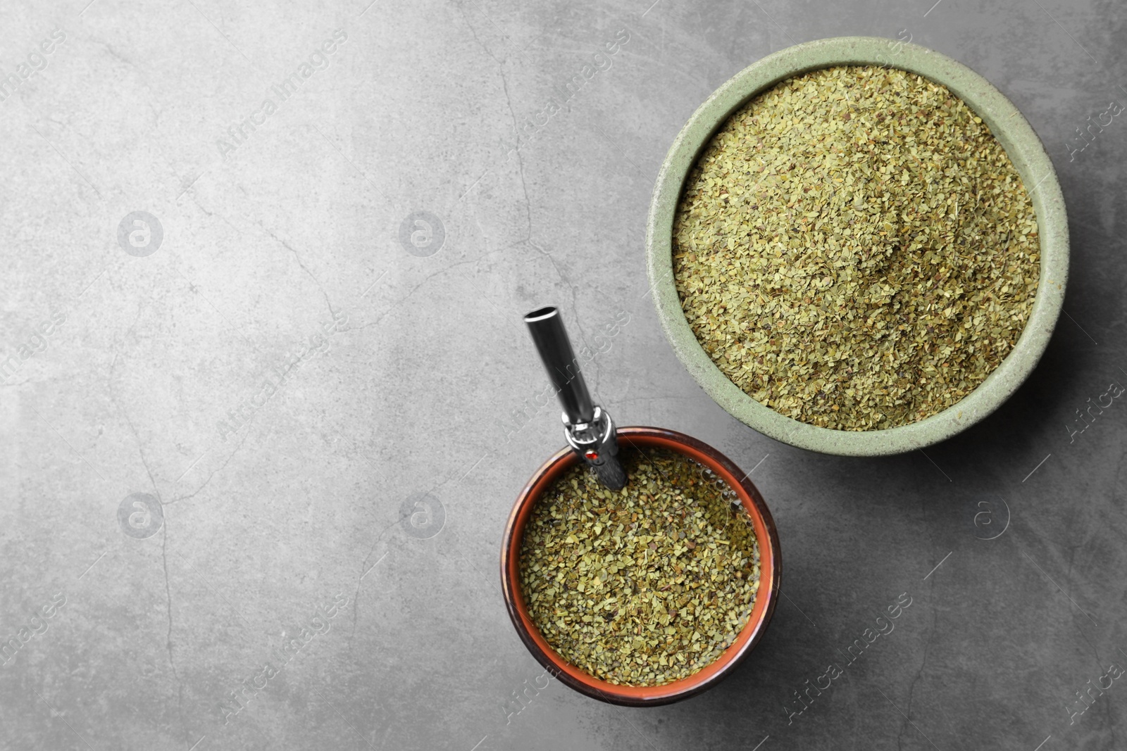 Photo of Guampa with bombilla and bowl of mate tea leaves on grey table, flat lay. Space for text