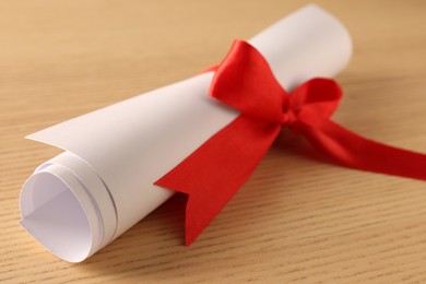 Graduation diploma tied with red ribbon on wooden table, closeup