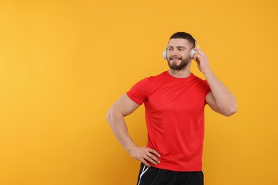 Handsome man with headphones on yellow background, space for text