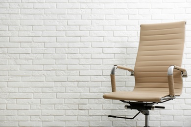 Comfortable office chair near white brick wall. Space for text