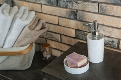 Dish with soap bars and bottle of shampoo on table near brick wall. Space for text