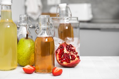 Tasty kombucha in glass bottles and fresh fruits on white tiled table, space for text