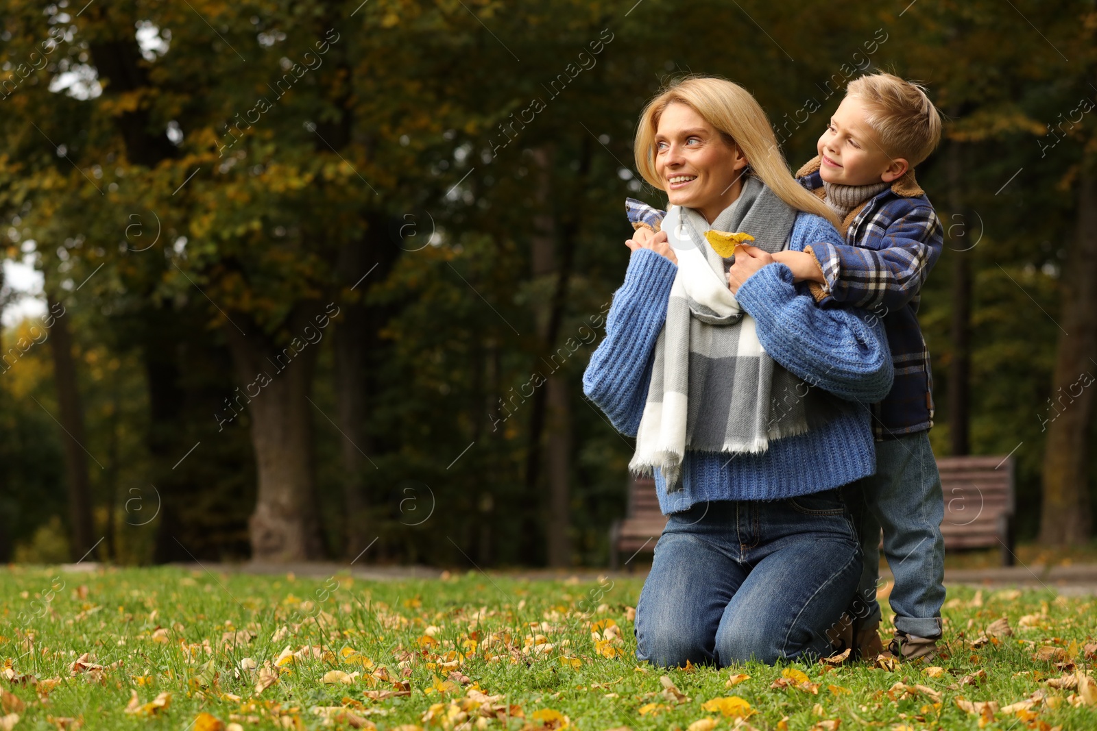 Photo of Happy mother with her son on green grass in autumn park. Space for text