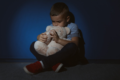 Photo of Sad little boy with teddy bear near blue wall. Domestic violence concept